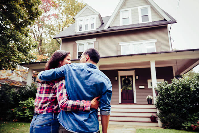 Einfamilienhaus kaufen – Zwei Personen die glücklich vor ihrem neuen Eigenheim stehen.