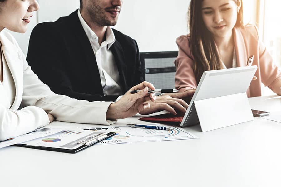 Drei Personen sitzen an einem Schreibtisch mit Dokumenten