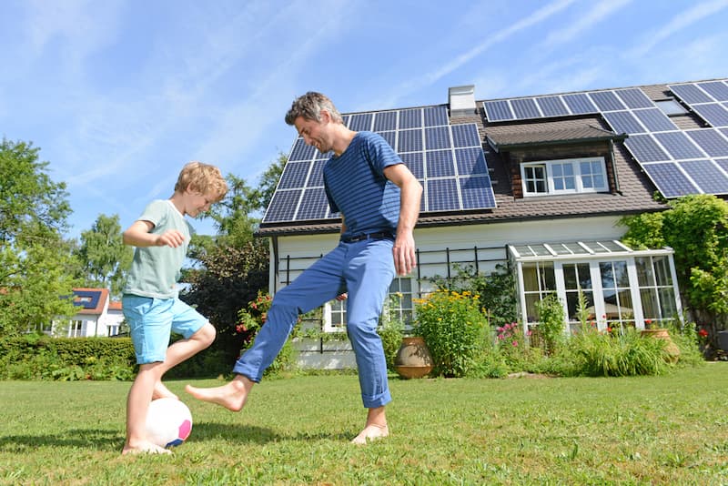 Ein Mann mit Kind vor einem Haus mit Solaranlagen auf dem Dach