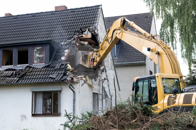 Ein Mensch lässt mit einem Bagger sein Haus abreißen