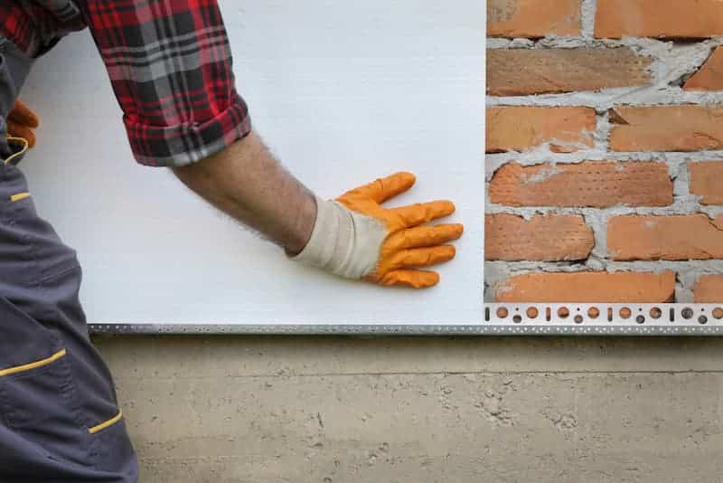 Ein Mann verlegt Platten, welche Arten von Fassadendämmung gibt es?
